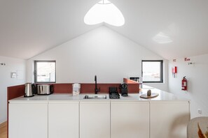 A modern kitchen with a white countertop, stainless steel appliances, and a red accent wall. - GuestReady - Joy Apartments - F (Porto)