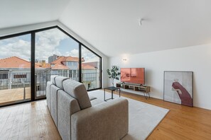A modern living room with a large window, a sofa, a flat-screen TV, and a painting on the wall. - GuestReady - Joy Apartments - F (Porto)