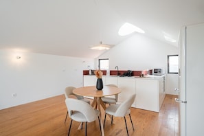 A modern kitchen with a dining area, featuring a round wooden table, four chairs, and a vase with dried flowers. - GuestReady - Joy Apartments - F (Porto)