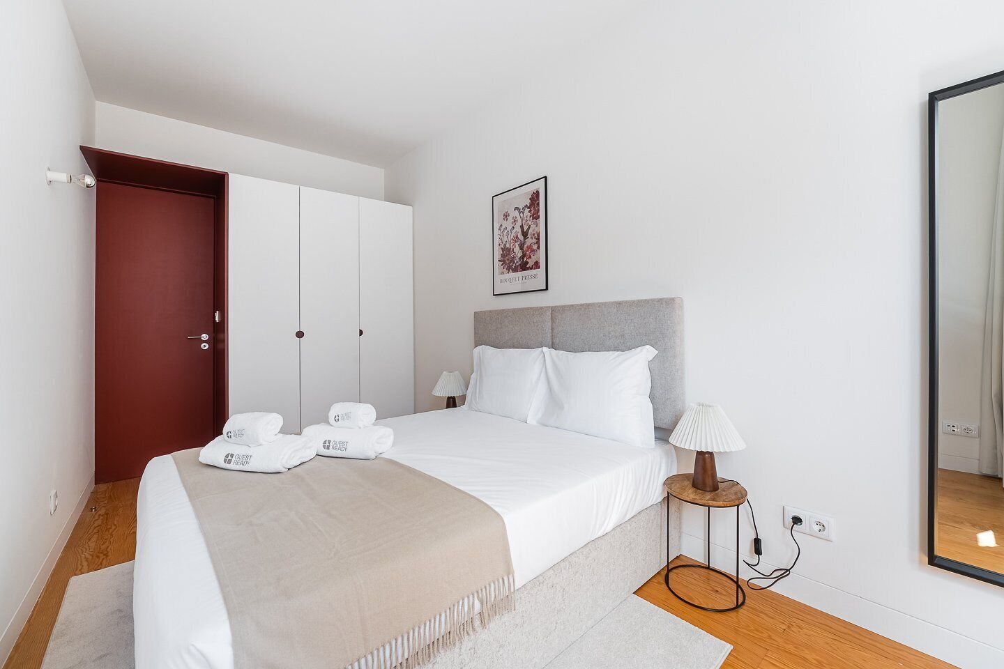 A hotel room with a bed, a bedside table with a lamp, a wardrobe, and a door.