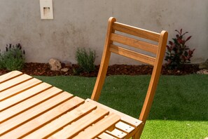 A wooden table and chair set outdoors with a grassy lawn and a wall in the background. - GuestReady - Joy Apartments - D (Porto)