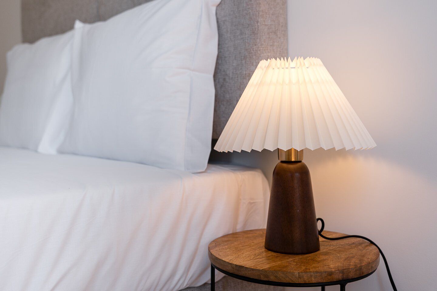 A bed with white bedding and a wooden bedside table with a lamp.