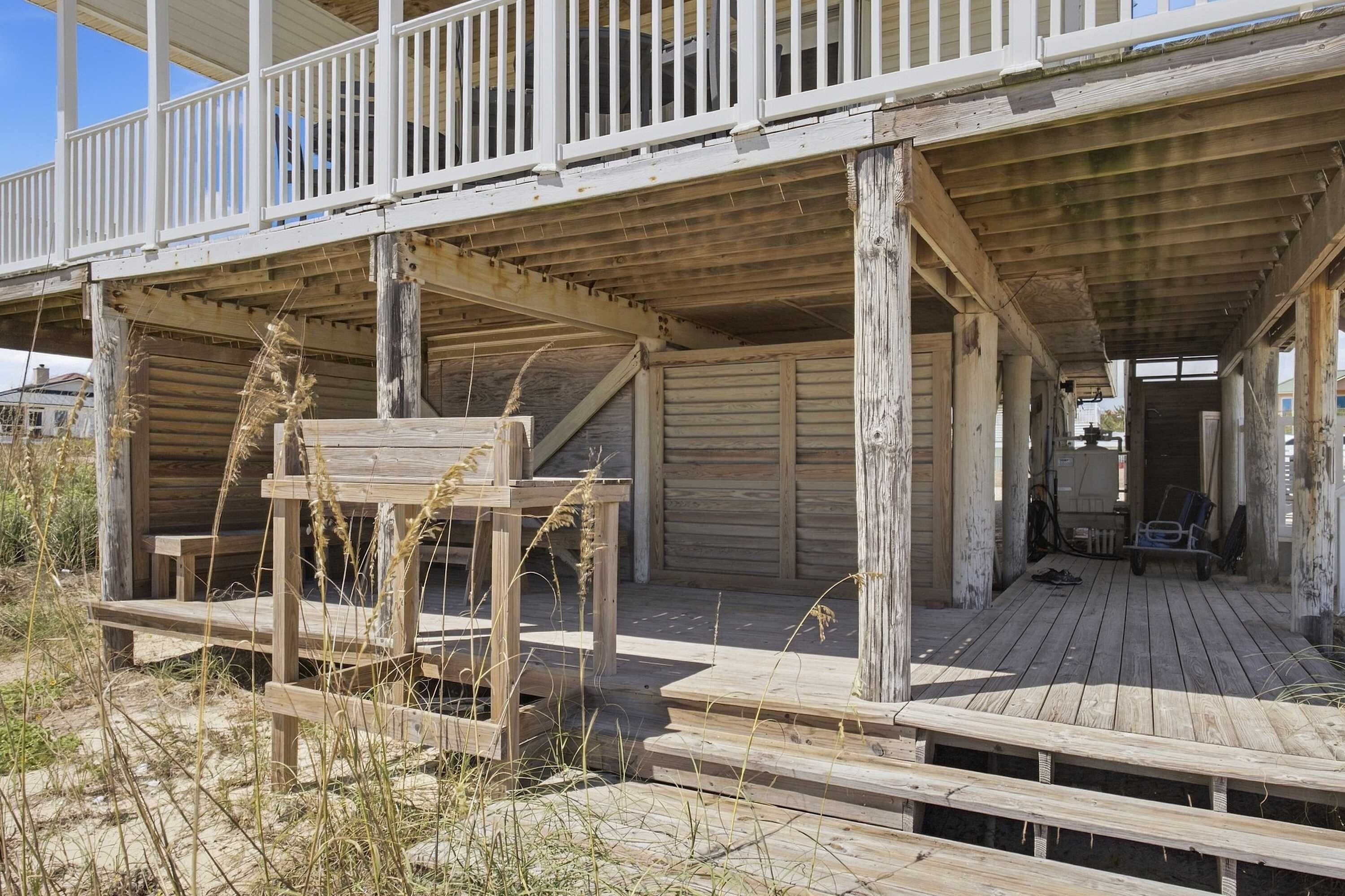 A wooden deck with a railing, a bench, and a covered area with a door leading inside.