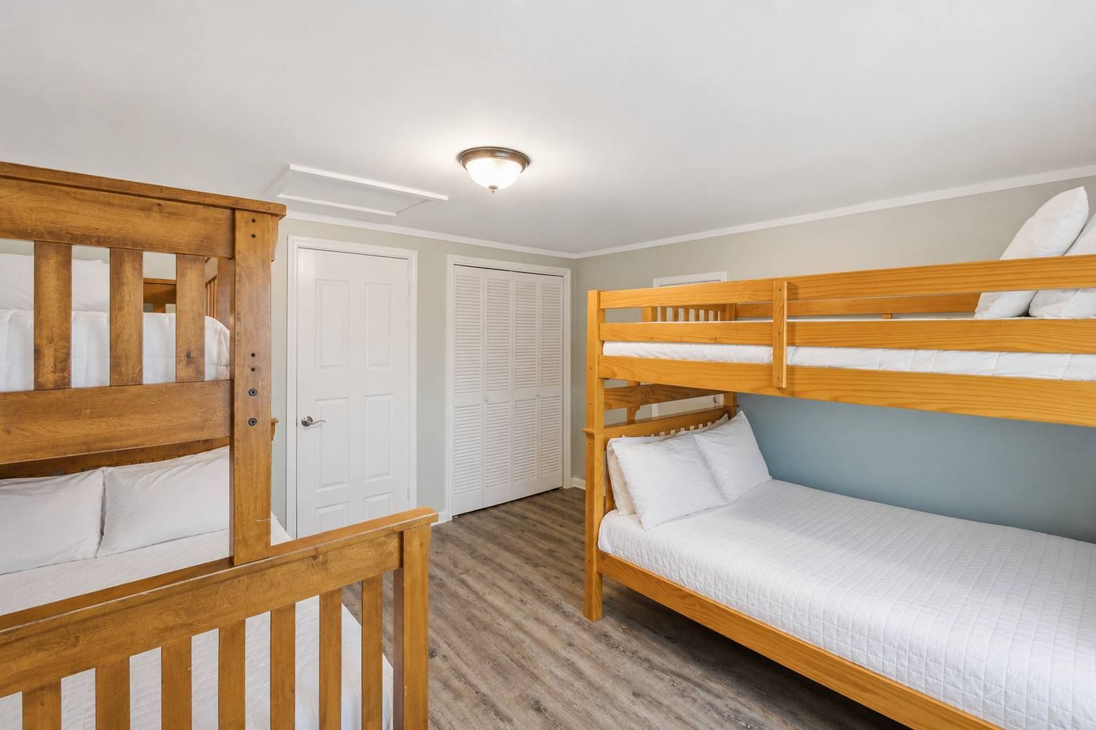 Une chambre avec un lit superposé, dotée d’une rambarde en bois, d’une porte blanche et d’un placard avec des portes coulissantes.