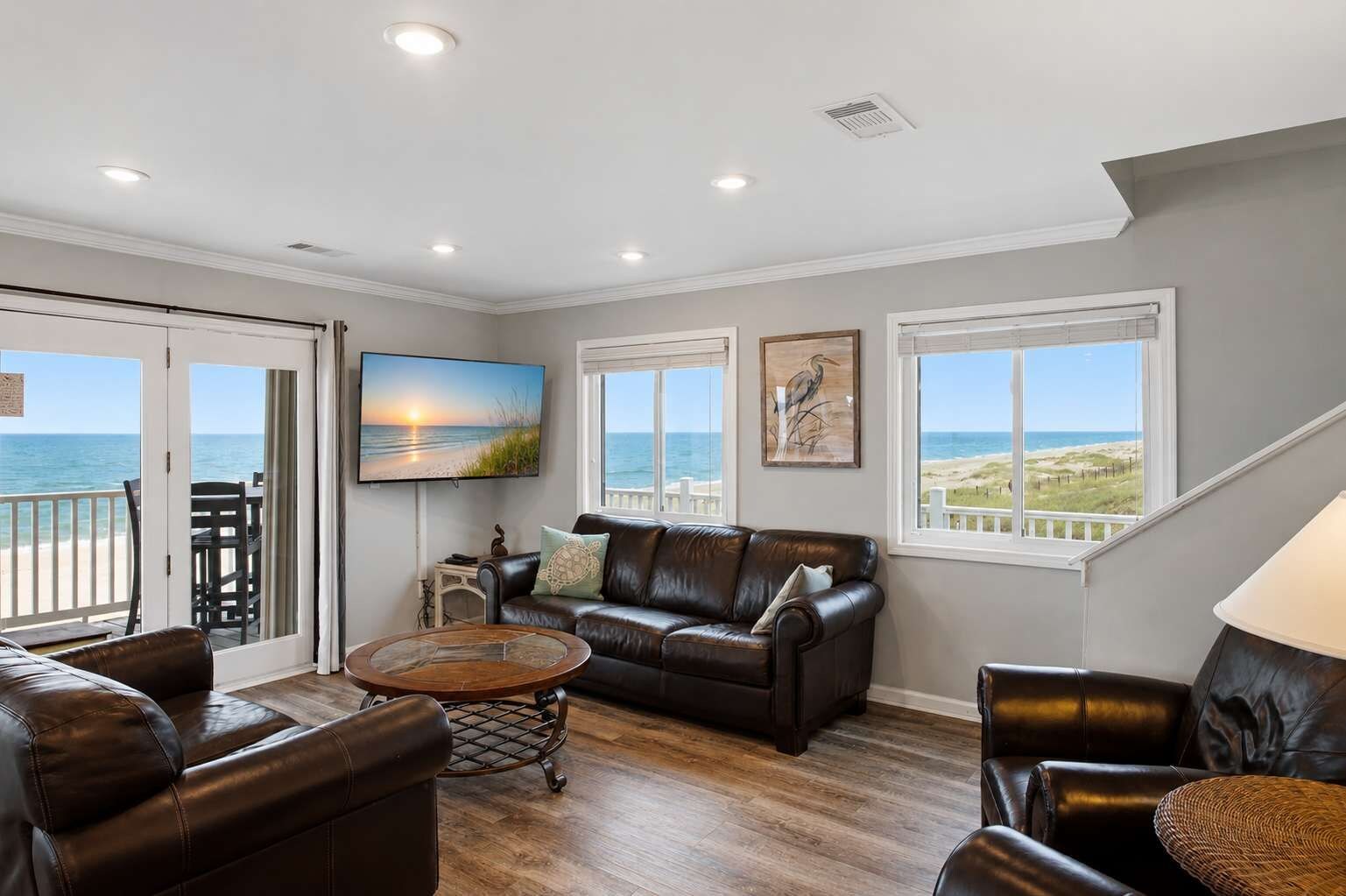 A living room with a leather sofa, a coffee table, and a TV displaying a sunset over the ocean.