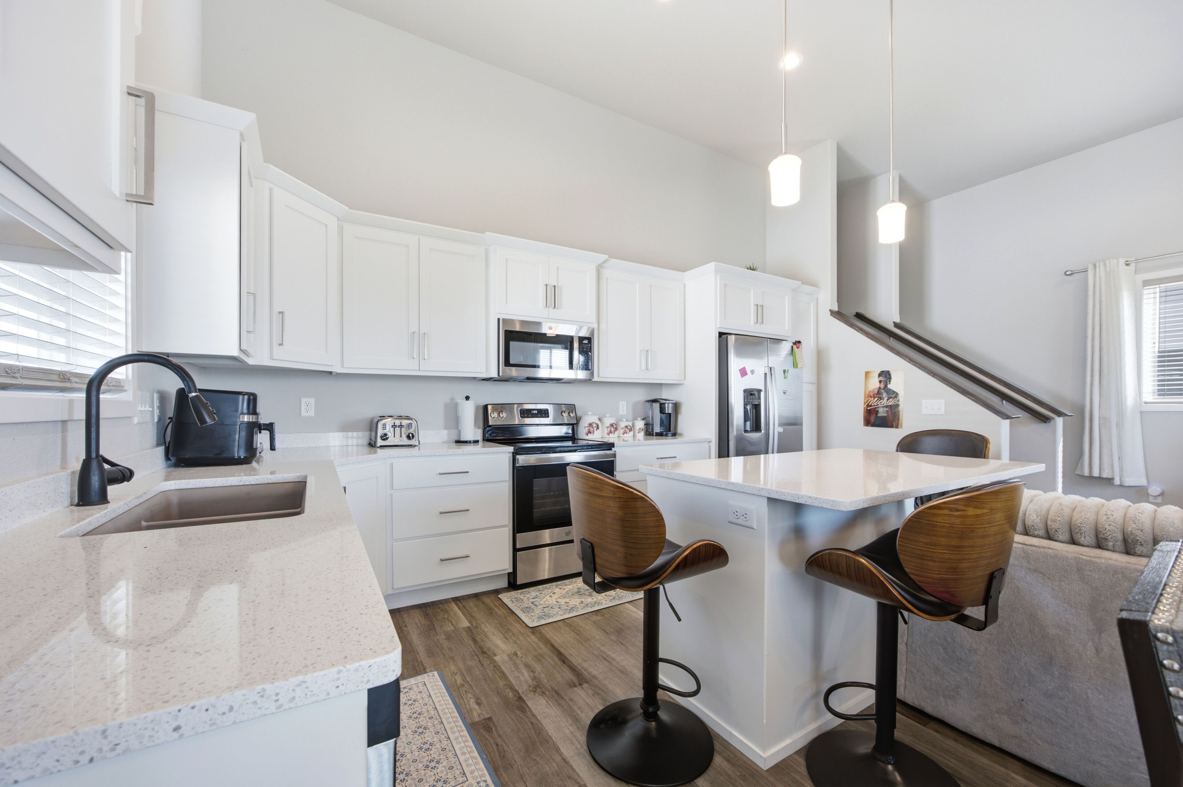 A modern kitchen with white cabinetry, stainless steel appliances, and a central island with bar stools.