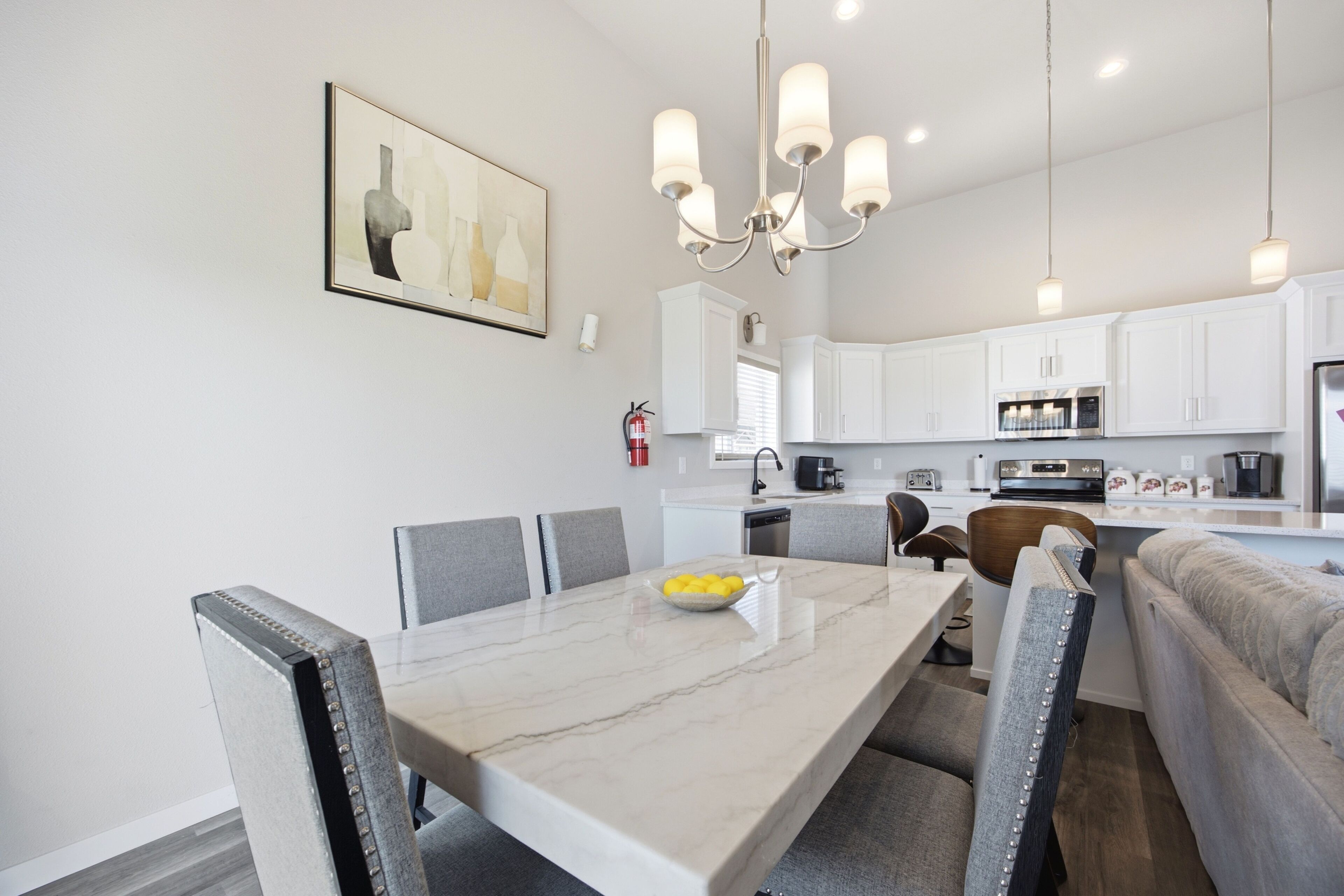 A modern kitchen with white cabinets, a dining table with chairs, and a chandelier.