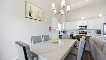 A modern kitchen with white cabinets, a dining table with chairs, and a chandelier.