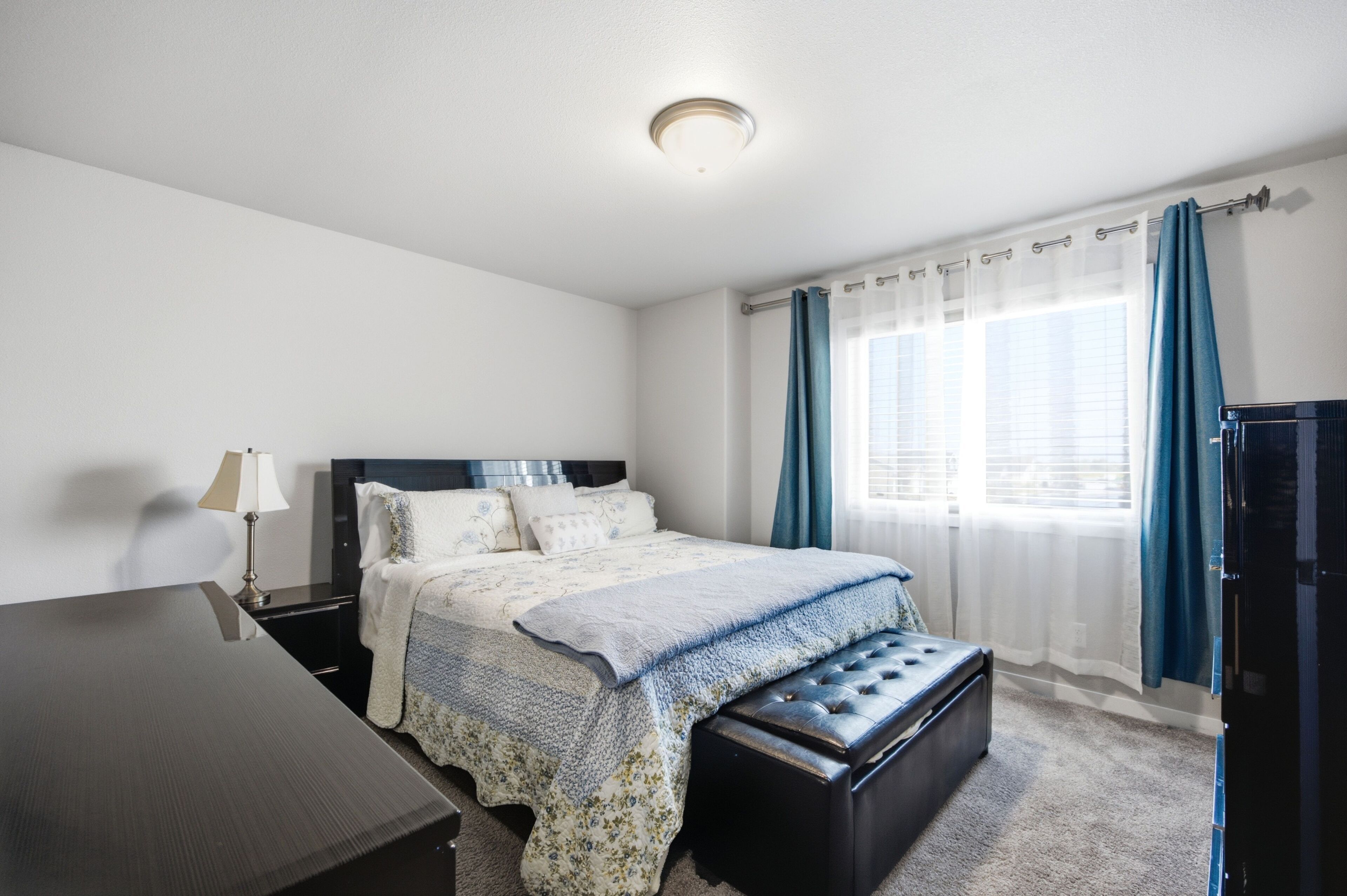 A bedroom with a bed, bedside table, lamp, and a window with curtains.