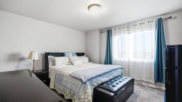 A bedroom with a bed, bedside table, lamp, and a window with curtains.