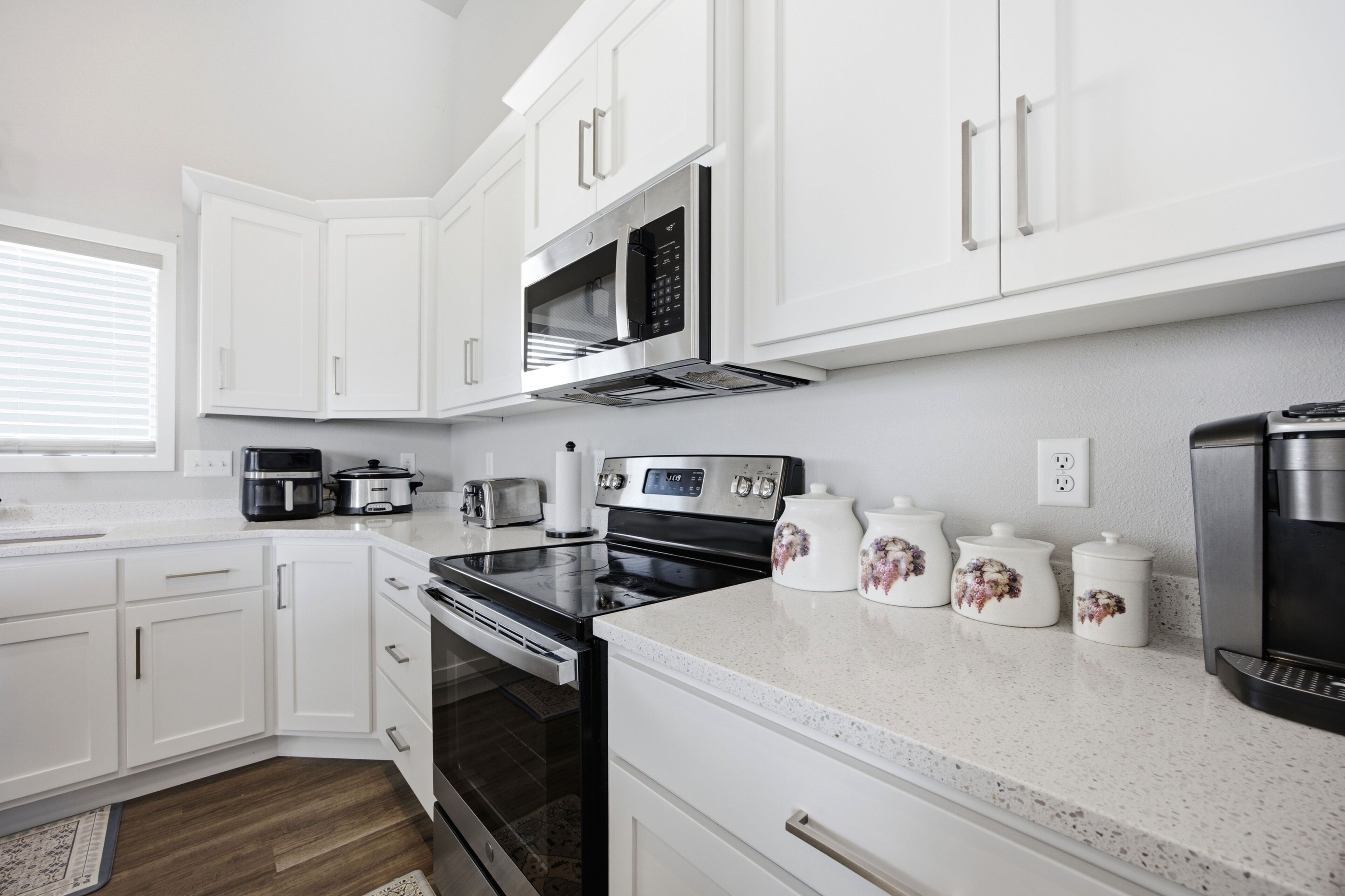 A modern kitchen with white cabinetry, a microwave, a stove, and a coffee maker.