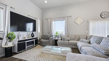 A modern living room with a flat-screen TV, a sofa set, a coffee table, and a decorative wall piece.