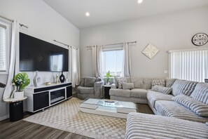 Una sala de estar moderna con un televisor de pantalla plana, un conjunto de sofás, una mesita de centro y un elemento decorativo en la pared.