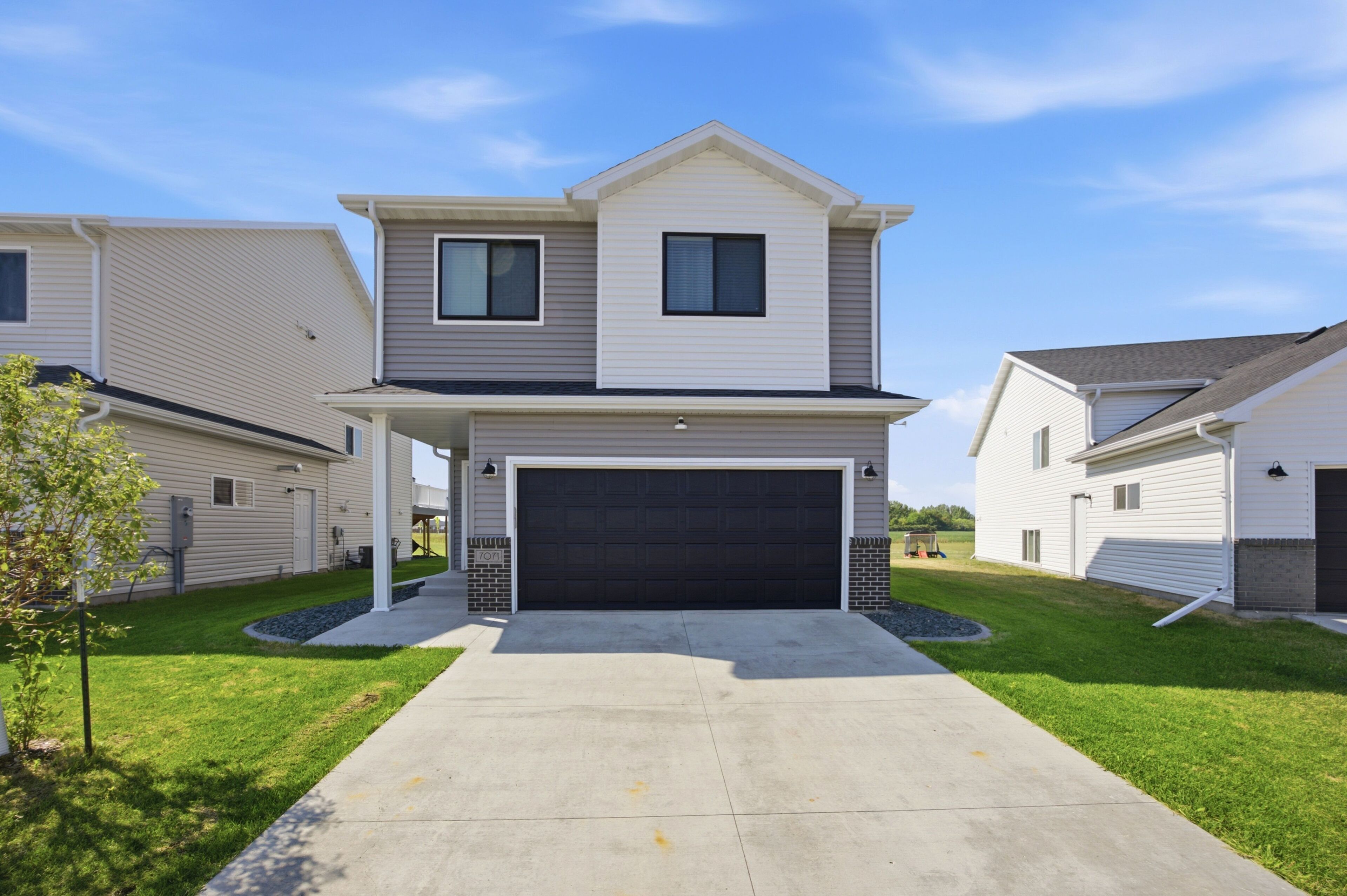 A two-story residential building with a garage, a covered porch, and a well-maintained lawn.