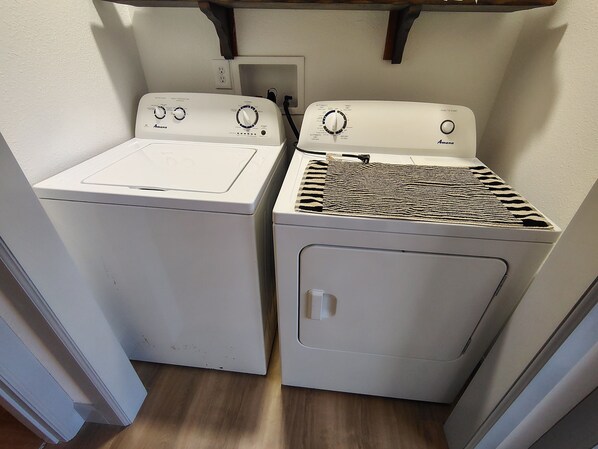 A laundry area with two white appliances, one with a flat surface and the other with a patterned top.