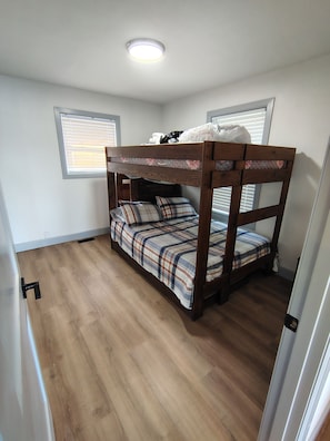 A bunk bed with a plaid bedspread, a wooden floor, and a ceiling light.