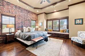 Ein Schlafzimmer mit Backsteinwand, einem Bett mit Sitzbank, einer Fensterbank und einem Sessel.