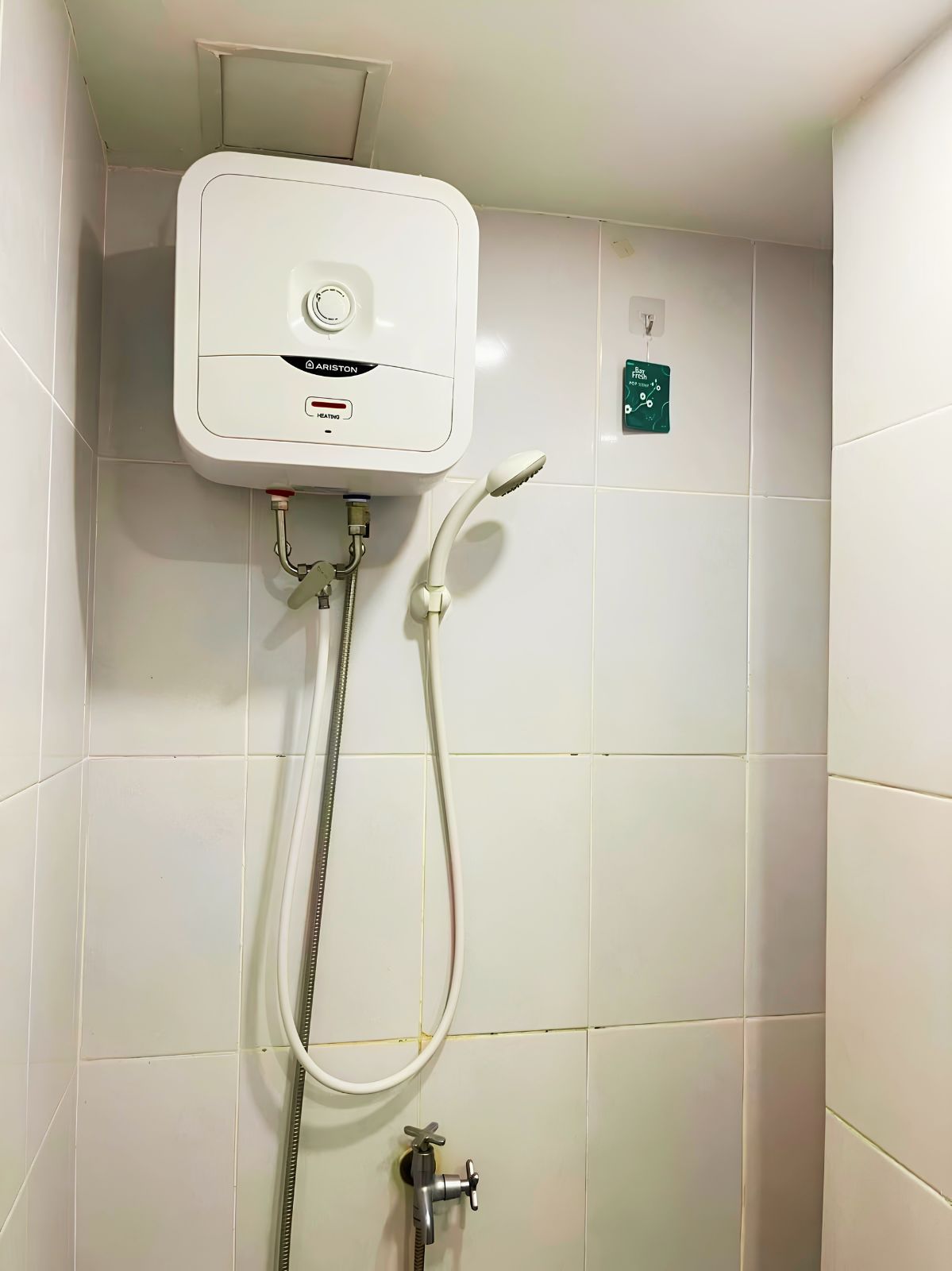 En vit väggmonterad dusch med en kontrollpanel, ett handhållet duschmunstycke och en separat kran.