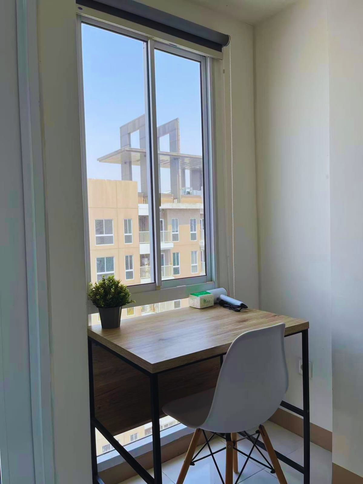 A corner room with a large window, a desk, a chair, and a potted plant.