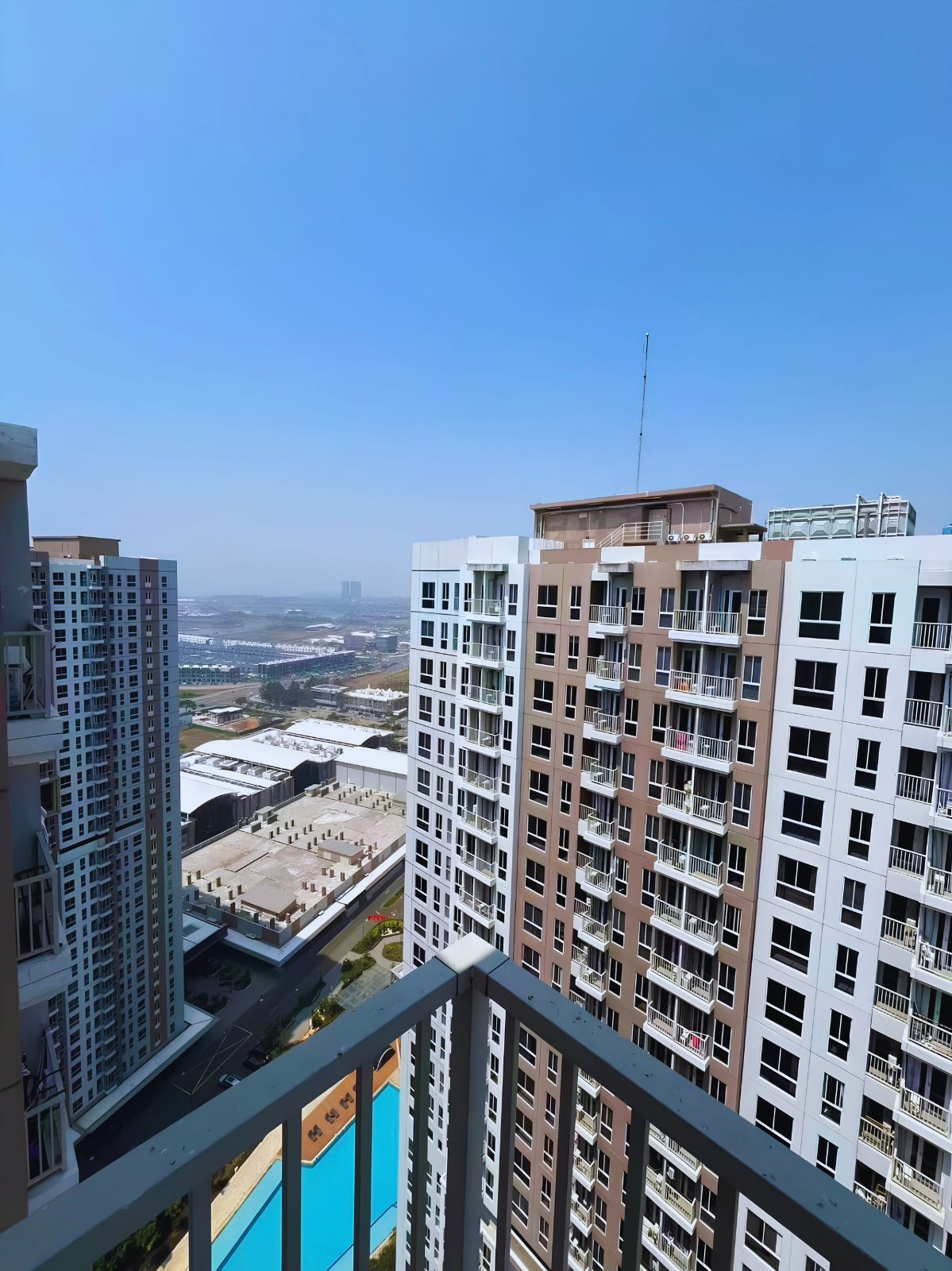 A high-rise residential building with multiple balconies, a clear view of the cityscape, and a distant body of water.