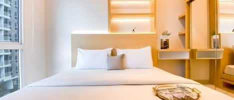 A hotel room with a bed, a bedside table, a magazine, and a window with a view of buildings.