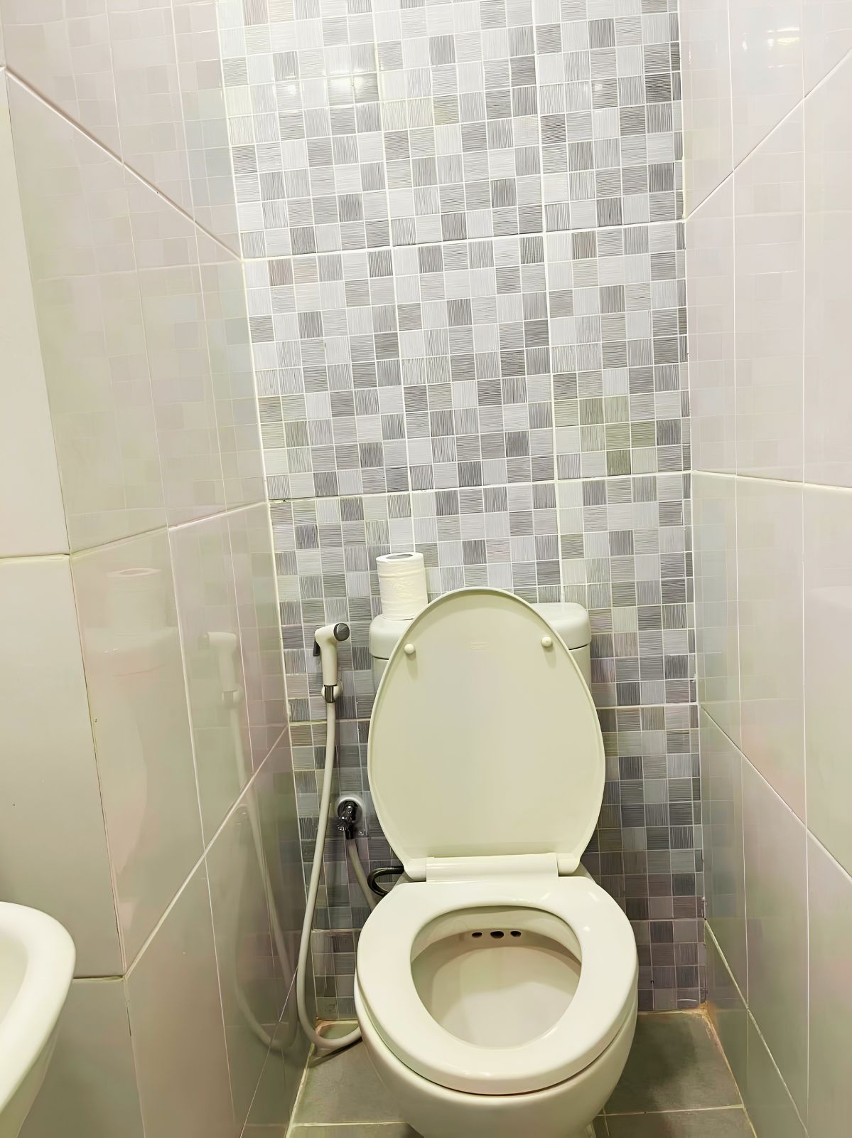 A bathroom with a toilet, a bidet, and a toilet paper holder on the wall.
