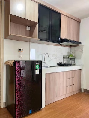 Una cocina con un refrigerador negro, armarios de madera, un lavamanos de acero inoxidable y una campana extractora negra.