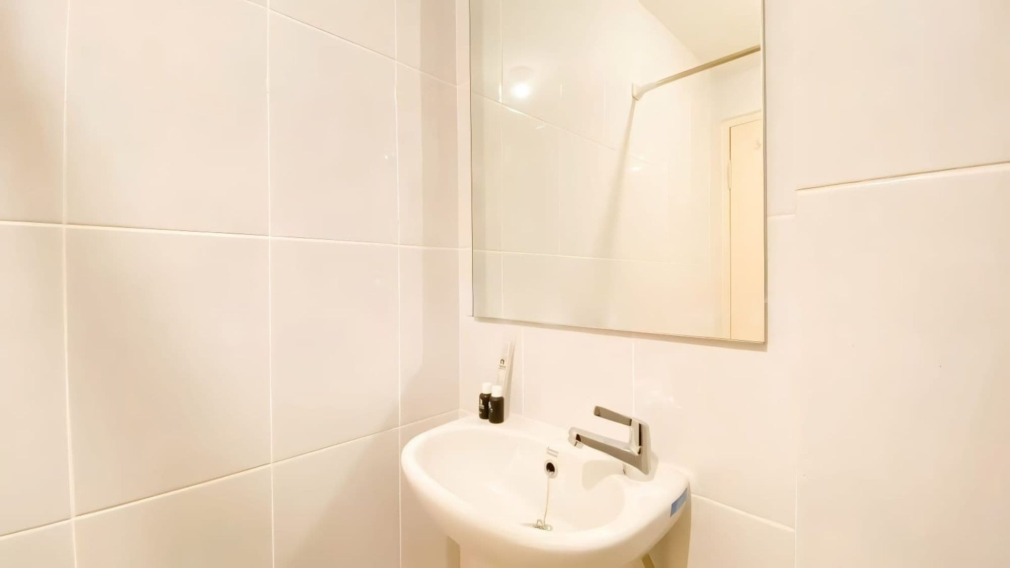 Un baño con azulejos blancos, un lavabo y un espejo.