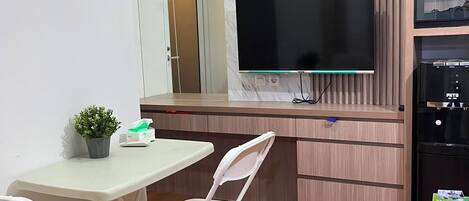 A compact kitchen with a flat-screen TV, a refrigerator, and a dining area with a table and chairs.