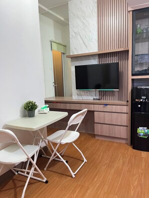 Una cocina compacta con televisión de pantalla plana, un refrigerador y un área de comedor con mesa y sillas.
