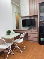 Una cocina compacta con televisión de pantalla plana, un refrigerador y un área de comedor con mesa y sillas.