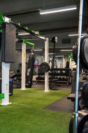 Ein Fitnessstudio mit verschiedenen Trainingsgeräten, darunter ein Sandsack, Gewichtsständer und eine Hantelbank.