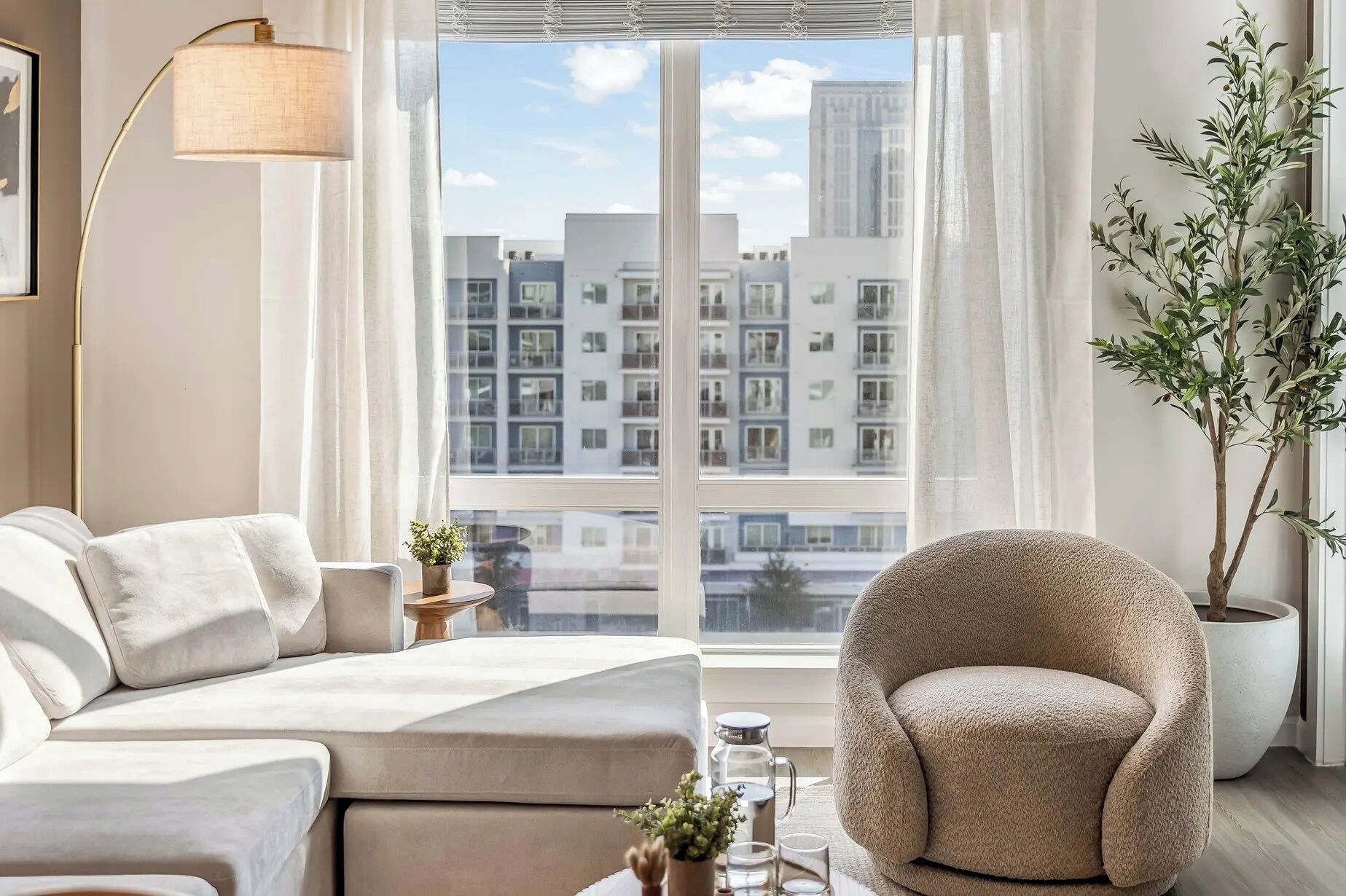 Ein modernes Wohnzimmer mit Sofa, Sessel und einem großen Fenster mit Blick auf die Stadt.