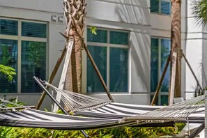A hammock set up between two palm trees in front of a building with large windows. - The Selena - Luxury Condo w/ Rooftop Pool, Gym (Orlando)