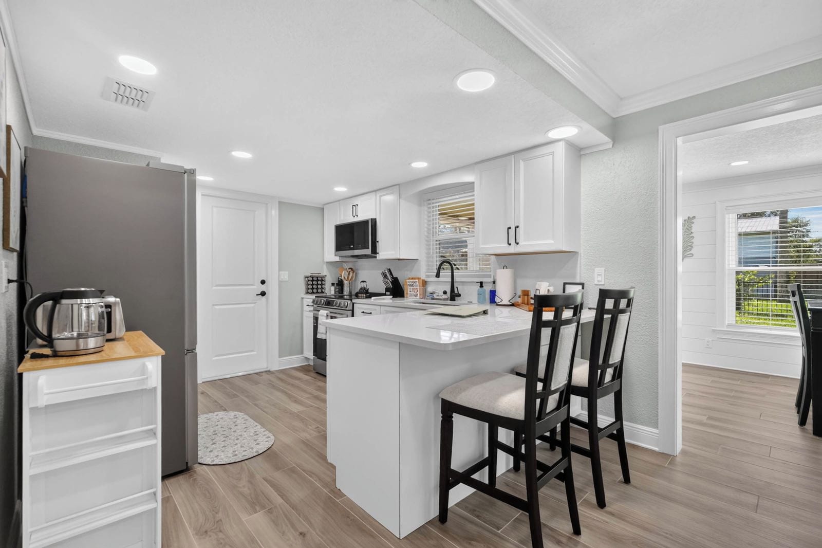 A modern kitchen with white cabinetry, a central island with bar stools, and a dining area with a table and chairs.