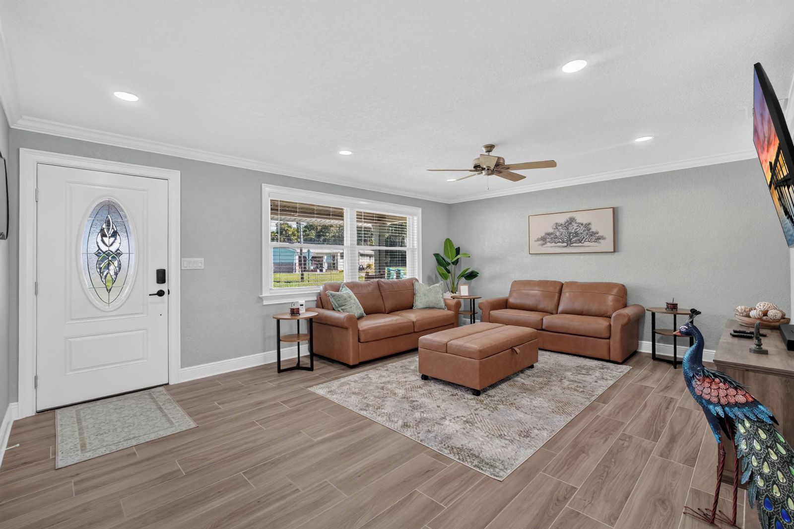 A living room with a brown leather sofa set, a peacock statue, and a ceiling fan.