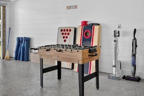 Ein Tischkicker in einem Raum mit weißer Wand, einem Staubsauger und einem Besen.