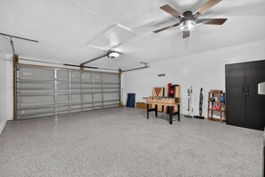 Uma garagem com porta fechada, ventilador de teto, mesa de pebolim e equipamentos esportivos.