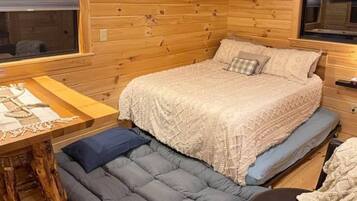 A cozy cabin interior with a bed, a small table, and a bench.