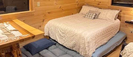 A cozy cabin interior with a bed, a small table, and a bench.