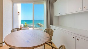 Una habitación con una mesa redonda de madera, sillas de mimbre, vista al mar y un armario blanco.