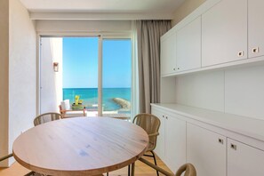 Ein Zimmer mit einem runden Holztisch, Korbstühlen, Blick aufs Meer und einem weißen Schrank.