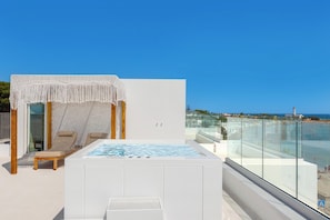A rooftop terrace with a hot tub, seating area, and a view of the beach.