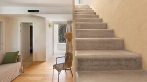 A staircase leading to an upper floor, a wicker chair, and a sofa in a room with wooden flooring and a view through a window.