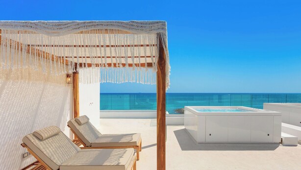 Un área de descanso frente al mar con piscina, sillones de madera y una pérgola.