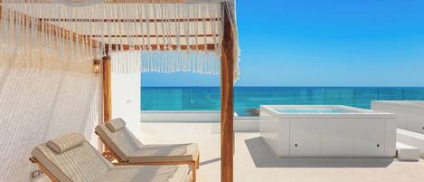 Un área de descanso frente al mar con piscina, sillones de madera y una pérgola.