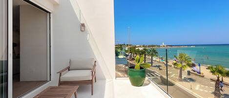 A balcony with a wooden bench, a potted plant, and a view of the beach and ocean.