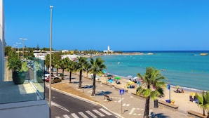 Vista costera con playa, palmeras y un faro a lo lejos.