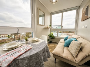 A modern living room with a dining area, large windows, and a view of the cityscape. - Oceana Suites Alamos  (Santiago)