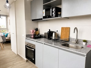 A modern kitchen with a built-in oven, a coffee maker, and a sink. - Oceana Suites Alamos  (Santiago)
